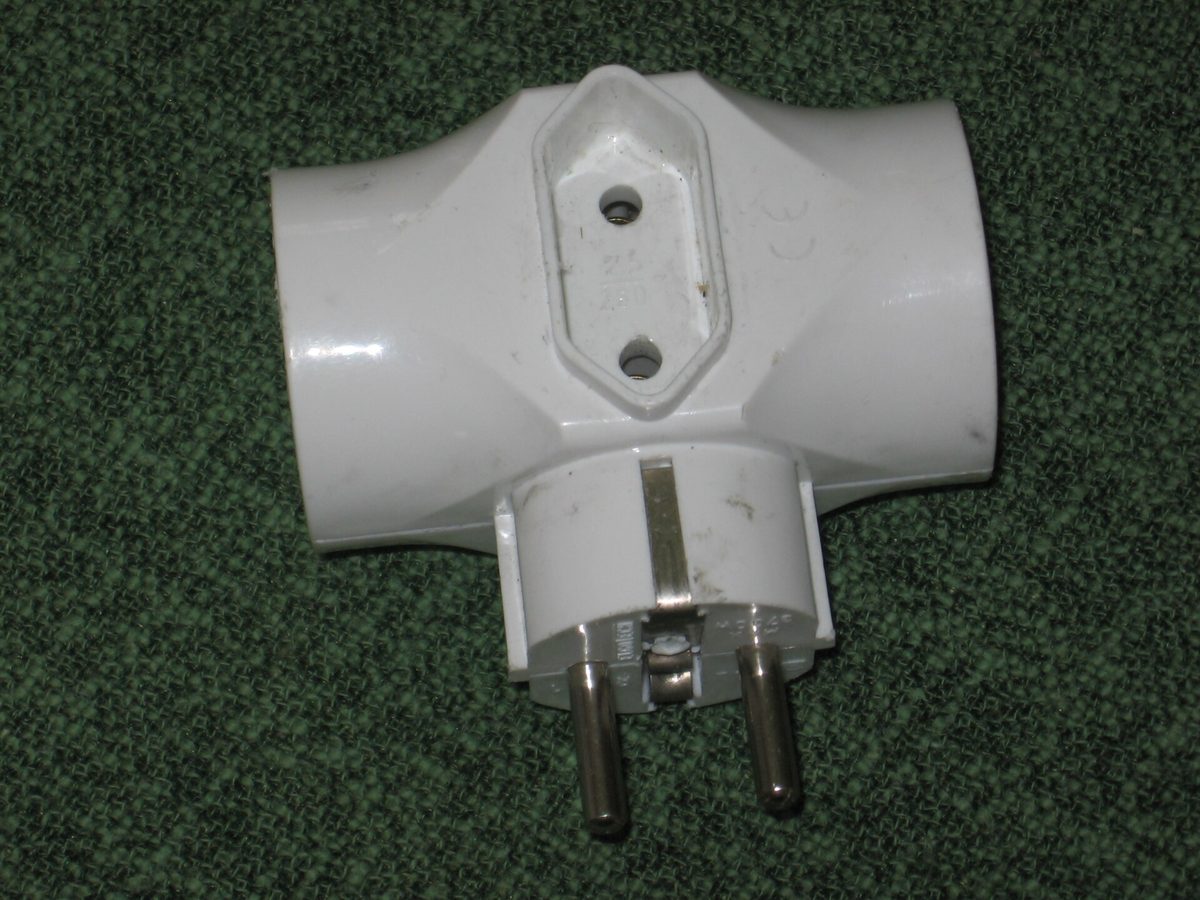 A white multi-way mains plug adapter photographed on a plain surface.