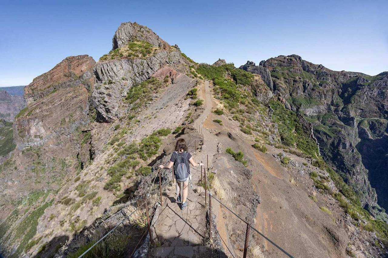 A hiker crossing a narrow rocky mountain ridge carrying a pack.