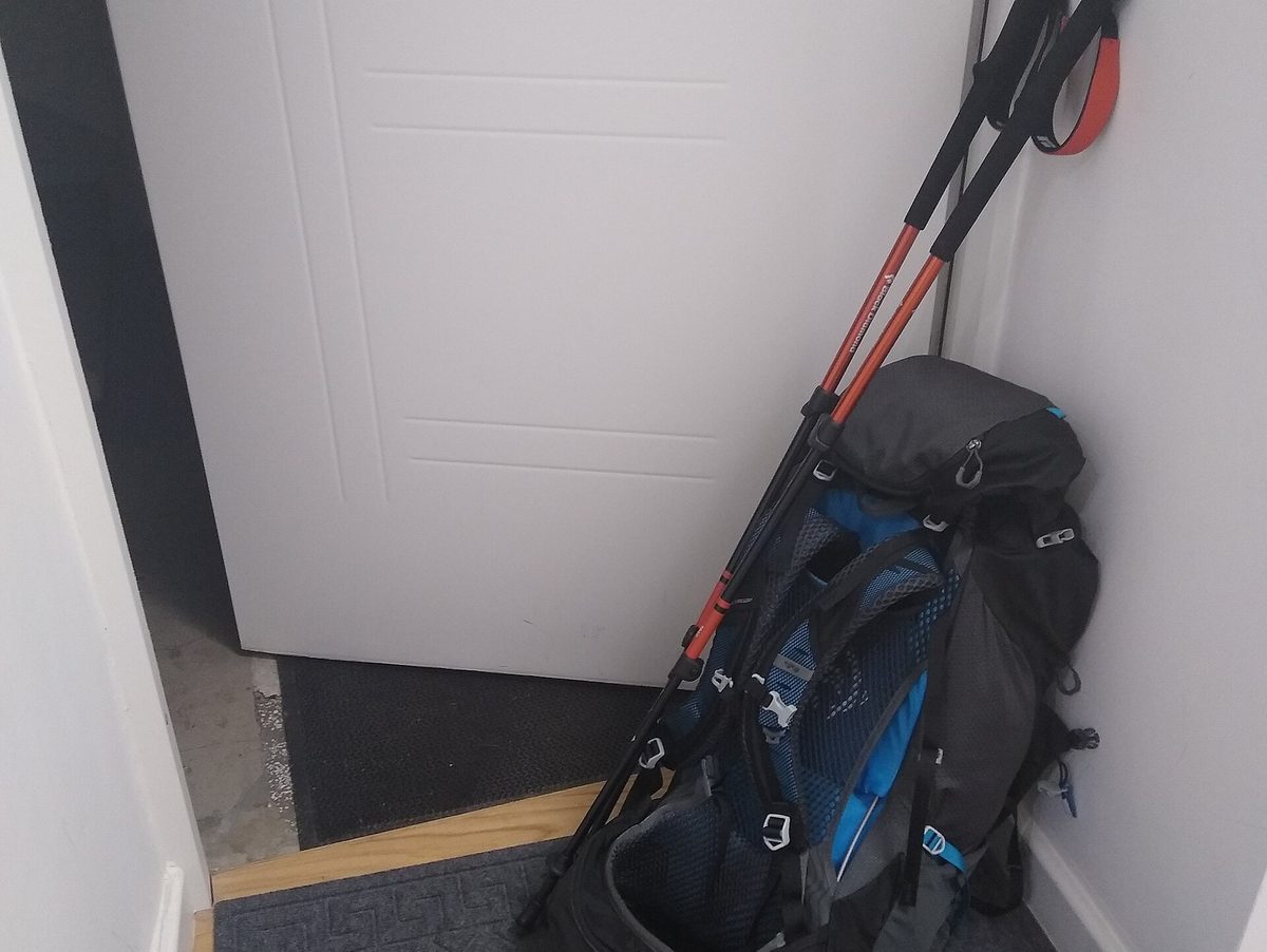 A loaded backpack with trekking poles standing upright against a wall.
