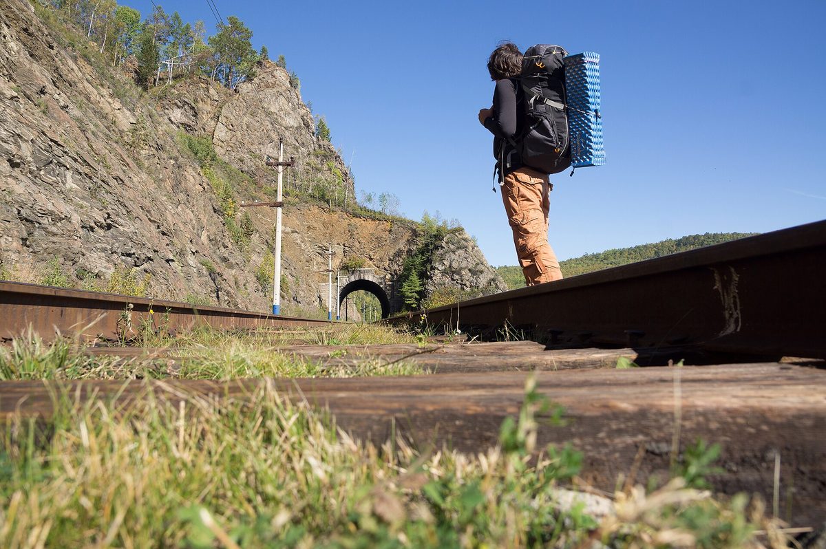 A traveller walking a railway line while carrying a large framed backpack.