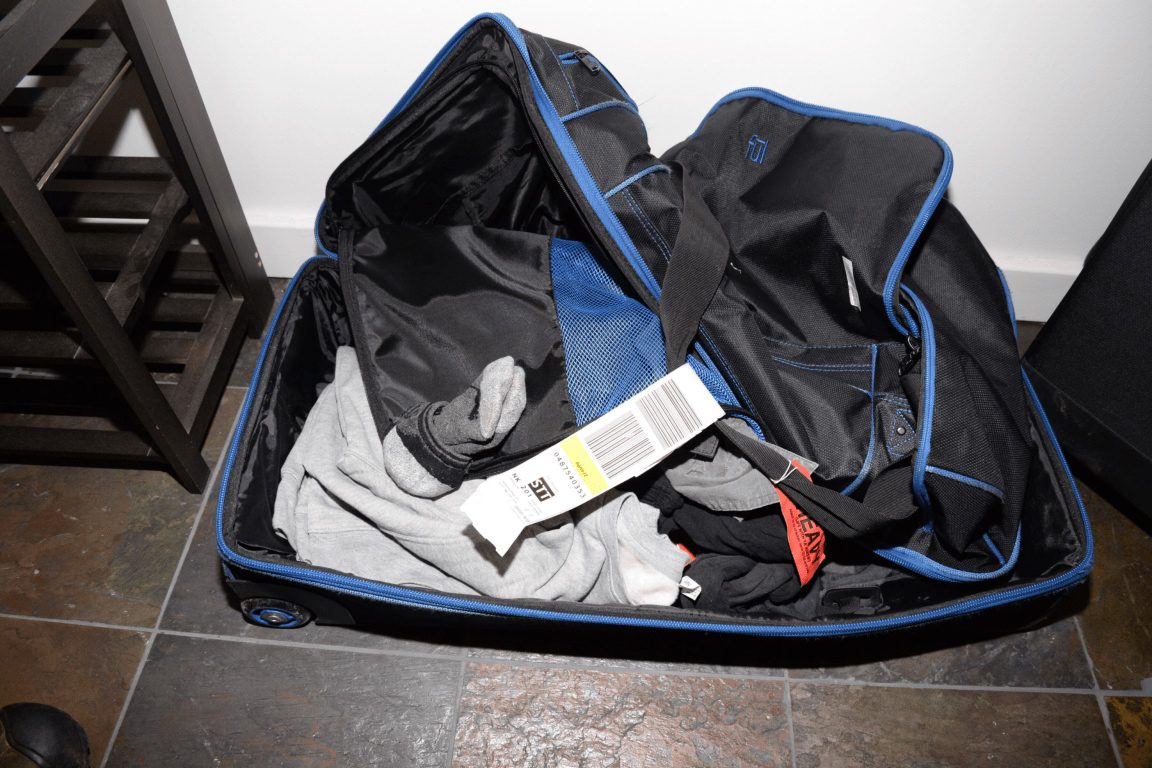 An open suitcase on the floor filled with folded clothes and tags.