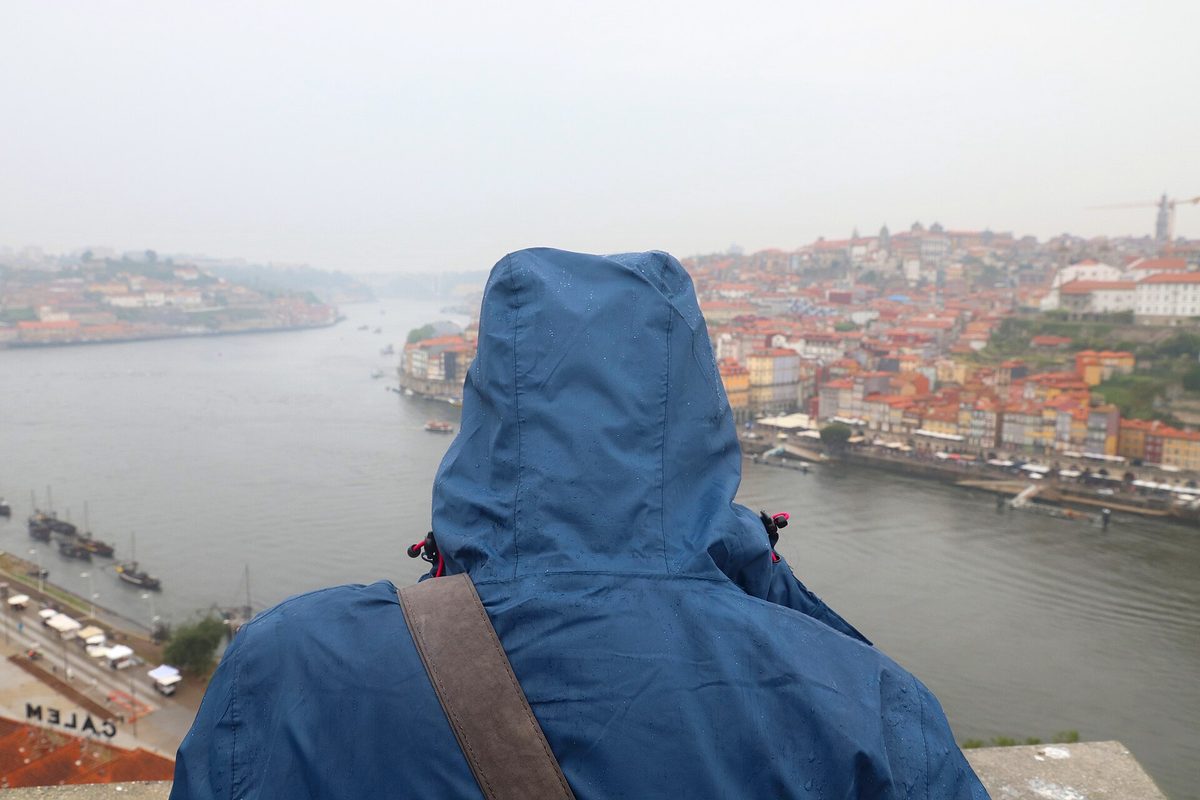A person in a hooded rain jacket seen from behind looking over a city in the rain.