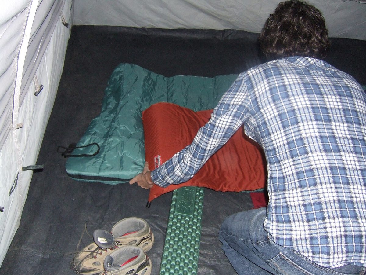 A camper adjusting a sleeping bag laid out on a pad inside a tent.